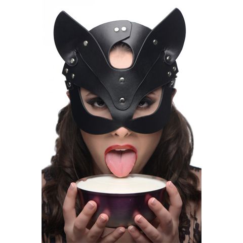 Woman in black leather cat mask licking from a bowl, representing fetish roleplay and animal play themes in bondage gear